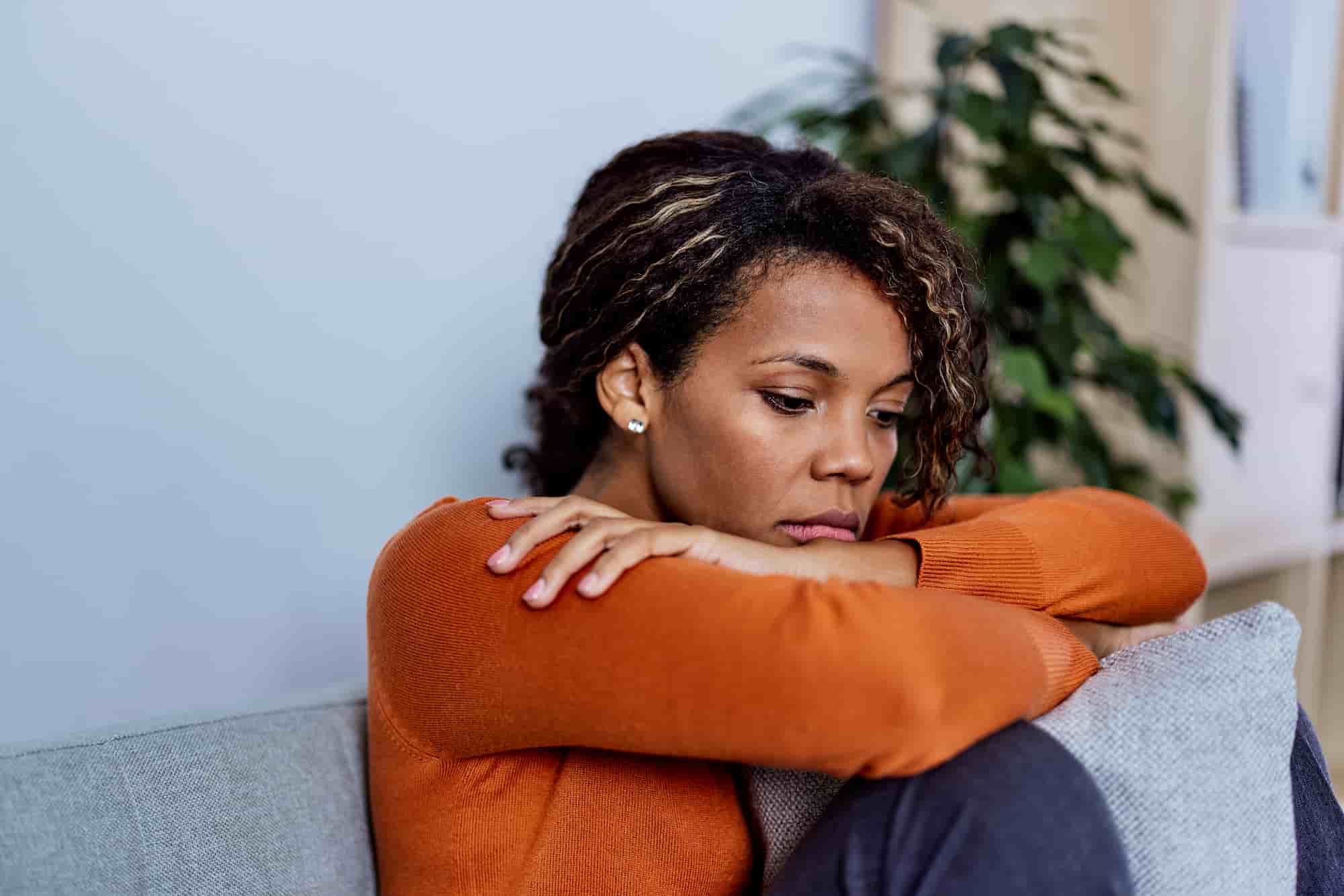 A woman sitting quietly and reflecting on a grey sofa in a calm, softly lit room