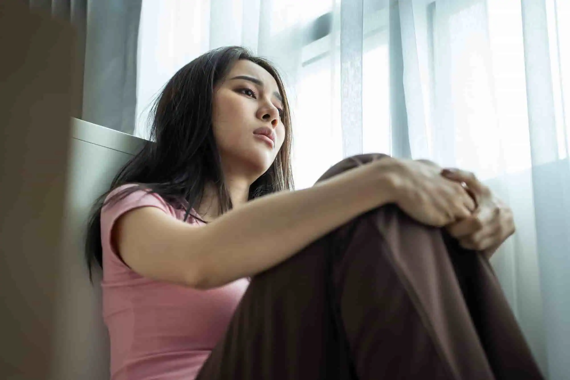 Woman sitting by a bedroom window looking thoughtful