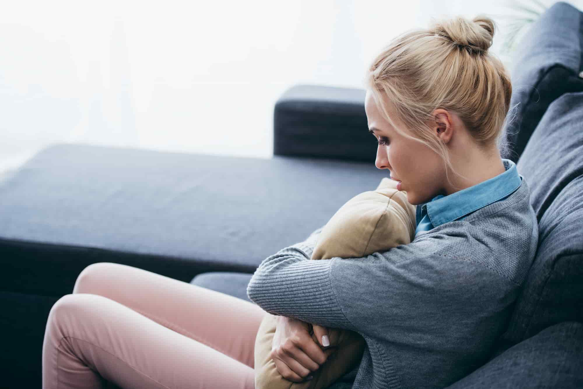 A woman holding a pillow while sitting on a grey couch in a calm, softly lit room
