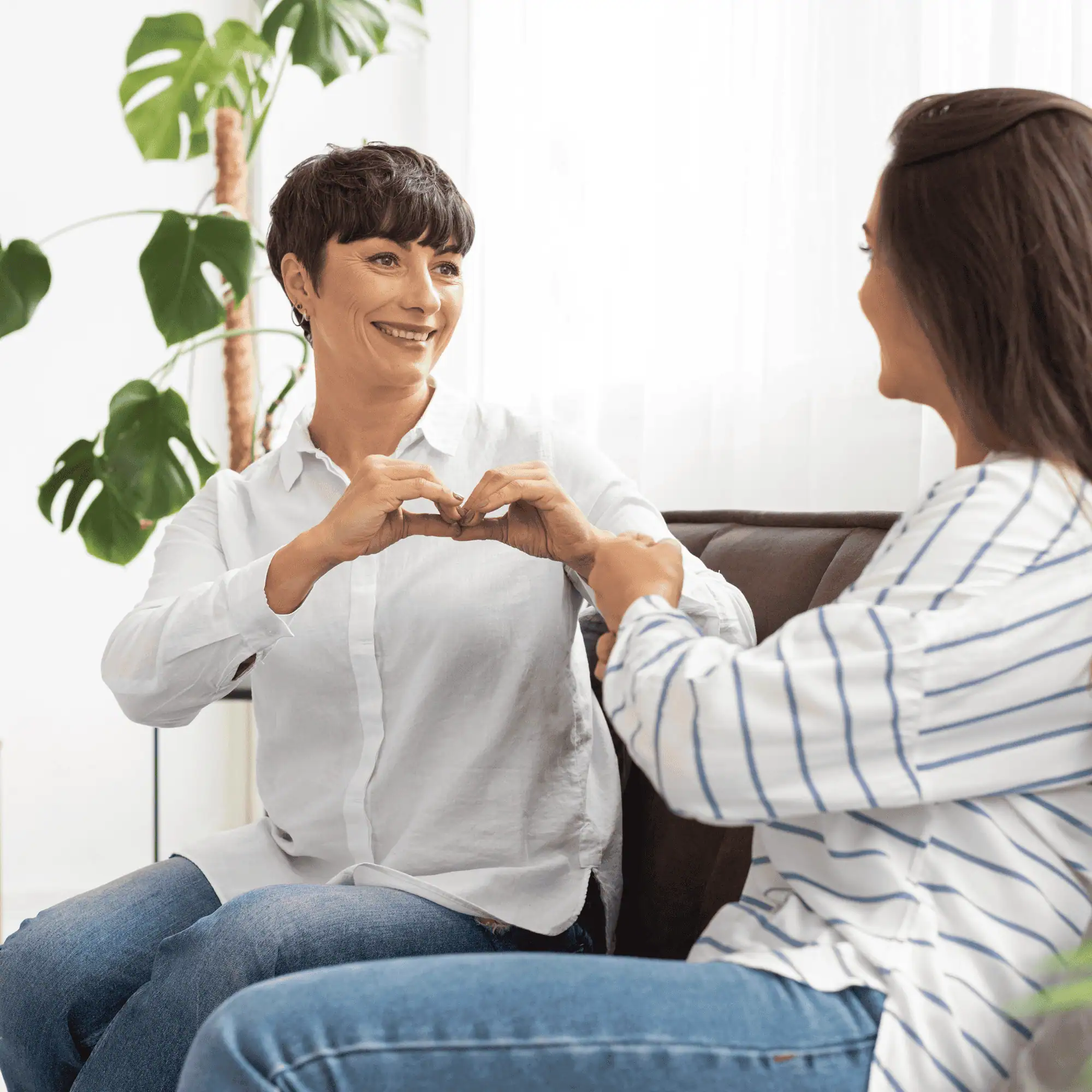 Women sharing a heartfelt moment in a cozy, well-lit room with green plants.