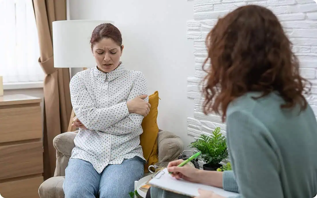 Woman in therapy session holding her arm, discussing health concerns.