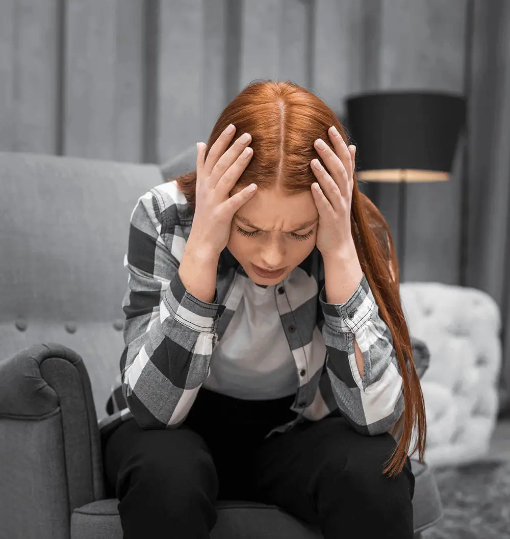 Woman with red hair holding her head in stress or pain at home.