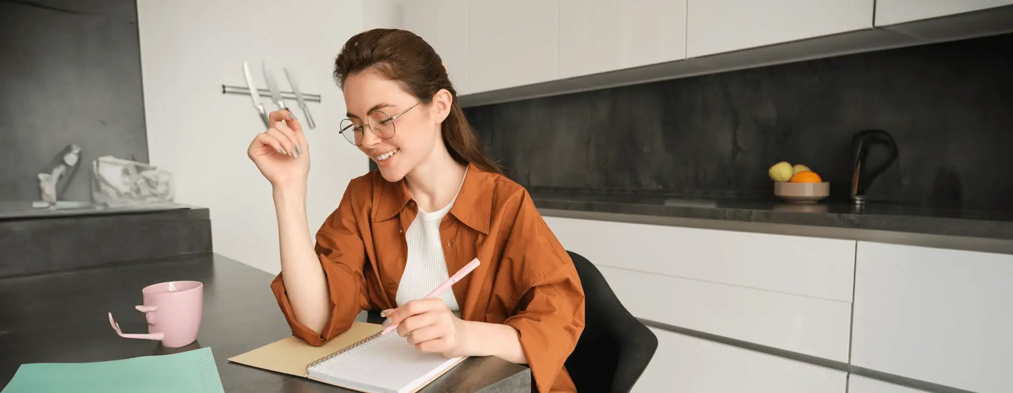 Young woman studying with a notebook and pen in a contemporary kitchen setting.