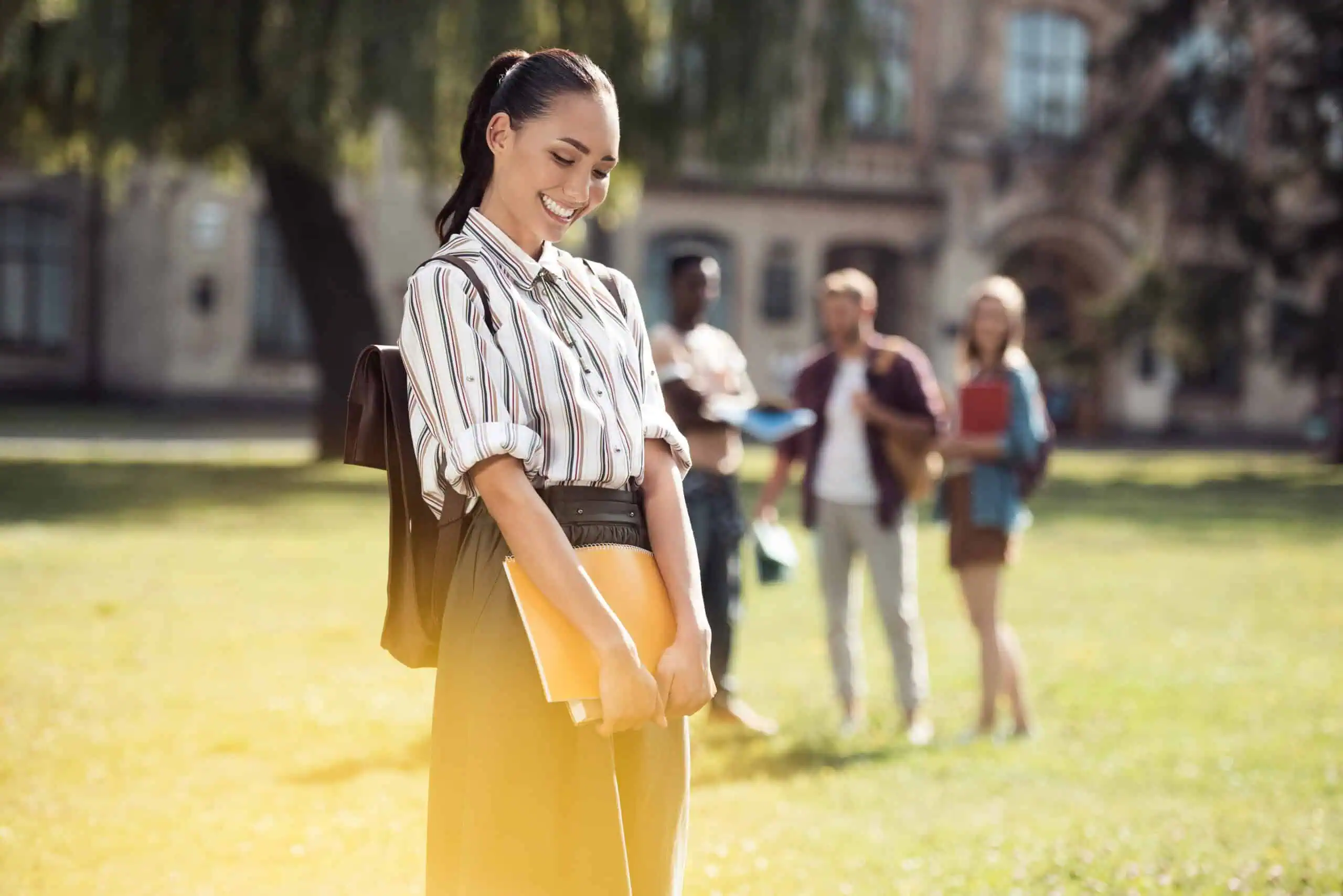 Young Asian college woman smiling and holding textbooks near UC Riverside