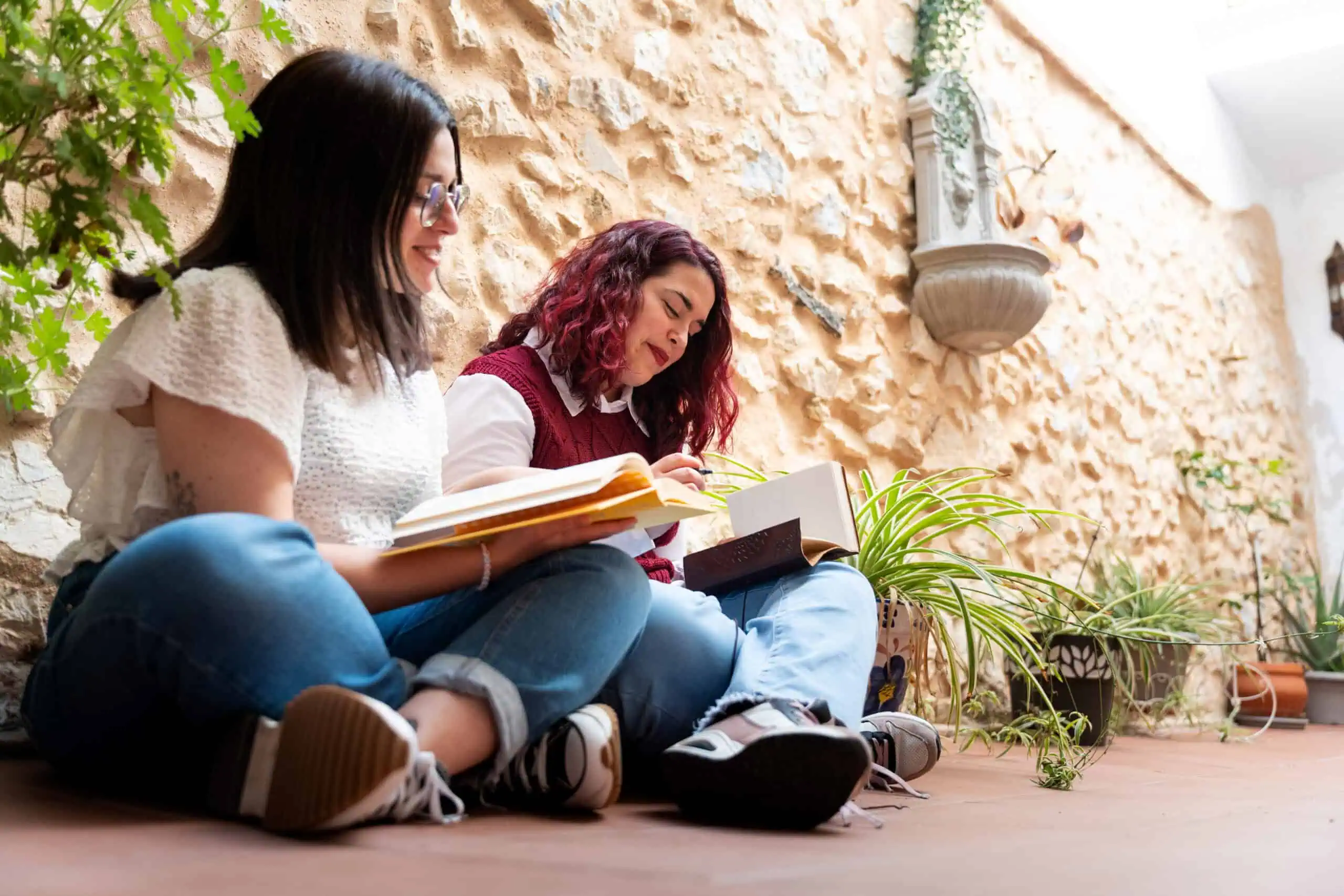 Two women sitting on the floor reading books outdoors at Sol Womens Treatment.