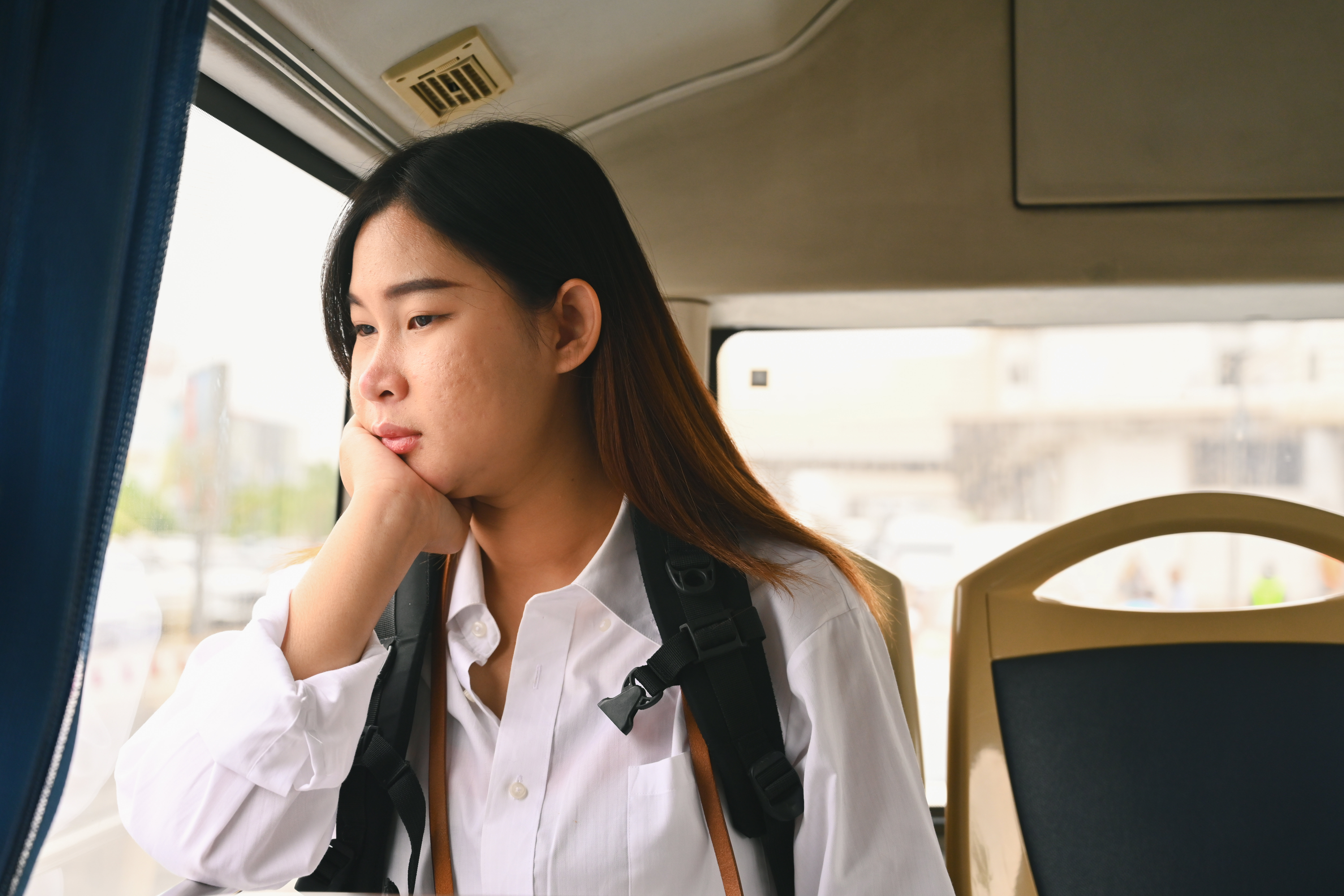 Female college student with a backpack looking out a bus window during a long Riverside commute
