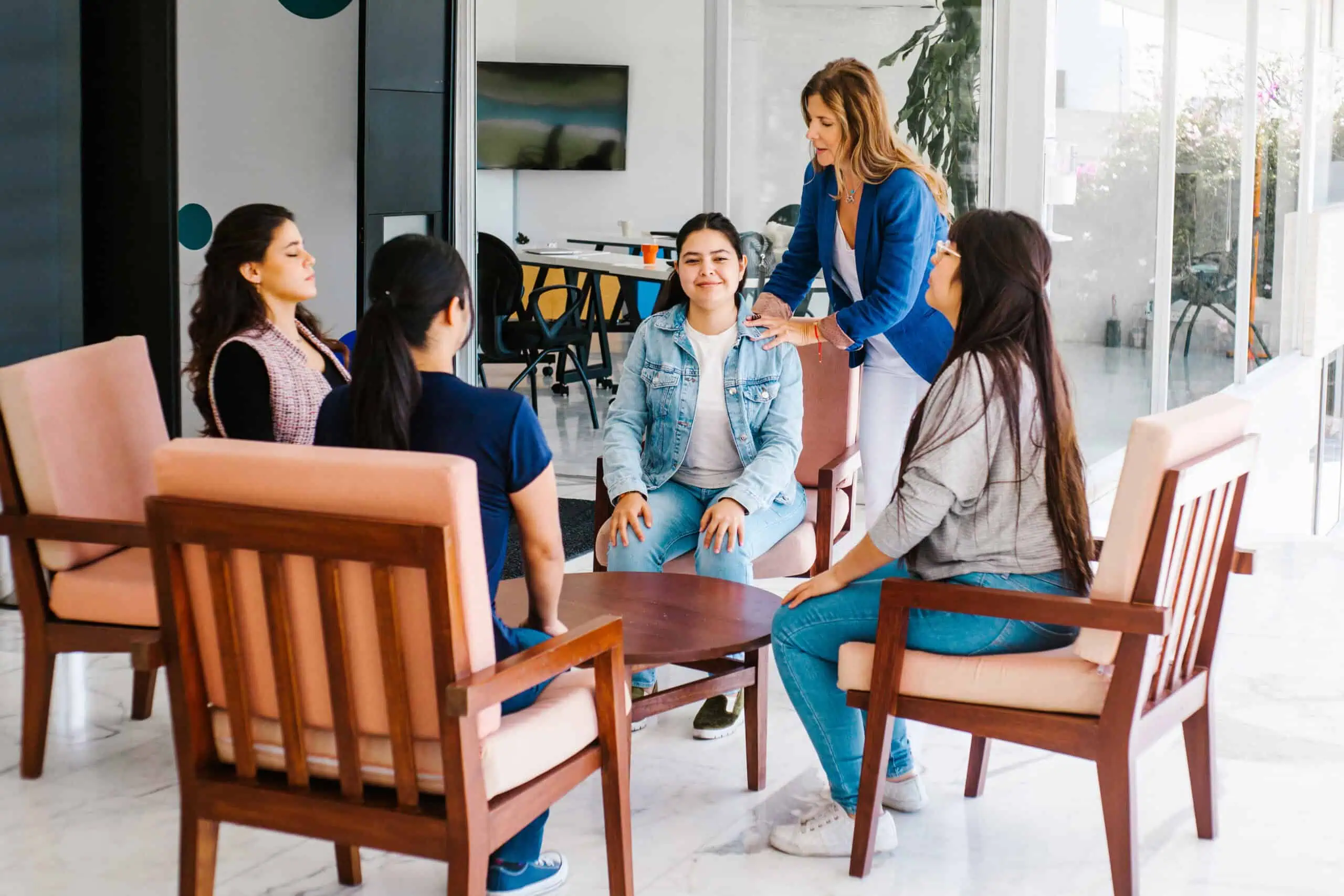 Women taking part in a group therapy session for mental health support, guided by a counselor in a calm, light-filled room